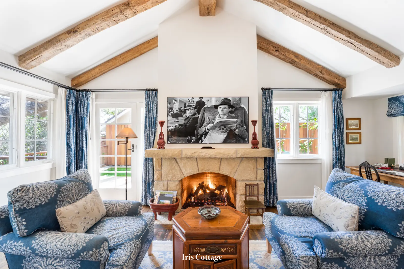 Iris: the stone fireplace lit between 2 blue floral armchairs, under exposed beams.