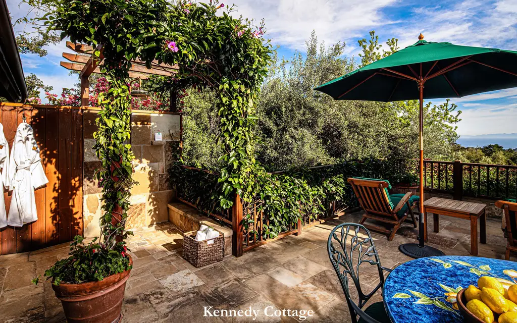 Kennedy: the stone terrace with its flowering pergola, a green parasol, a lounger and the ocean in the distance.