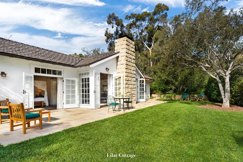 Lilac: the white cottage with its stone chimney, seen from the lawn, wooden chairs on the patio.