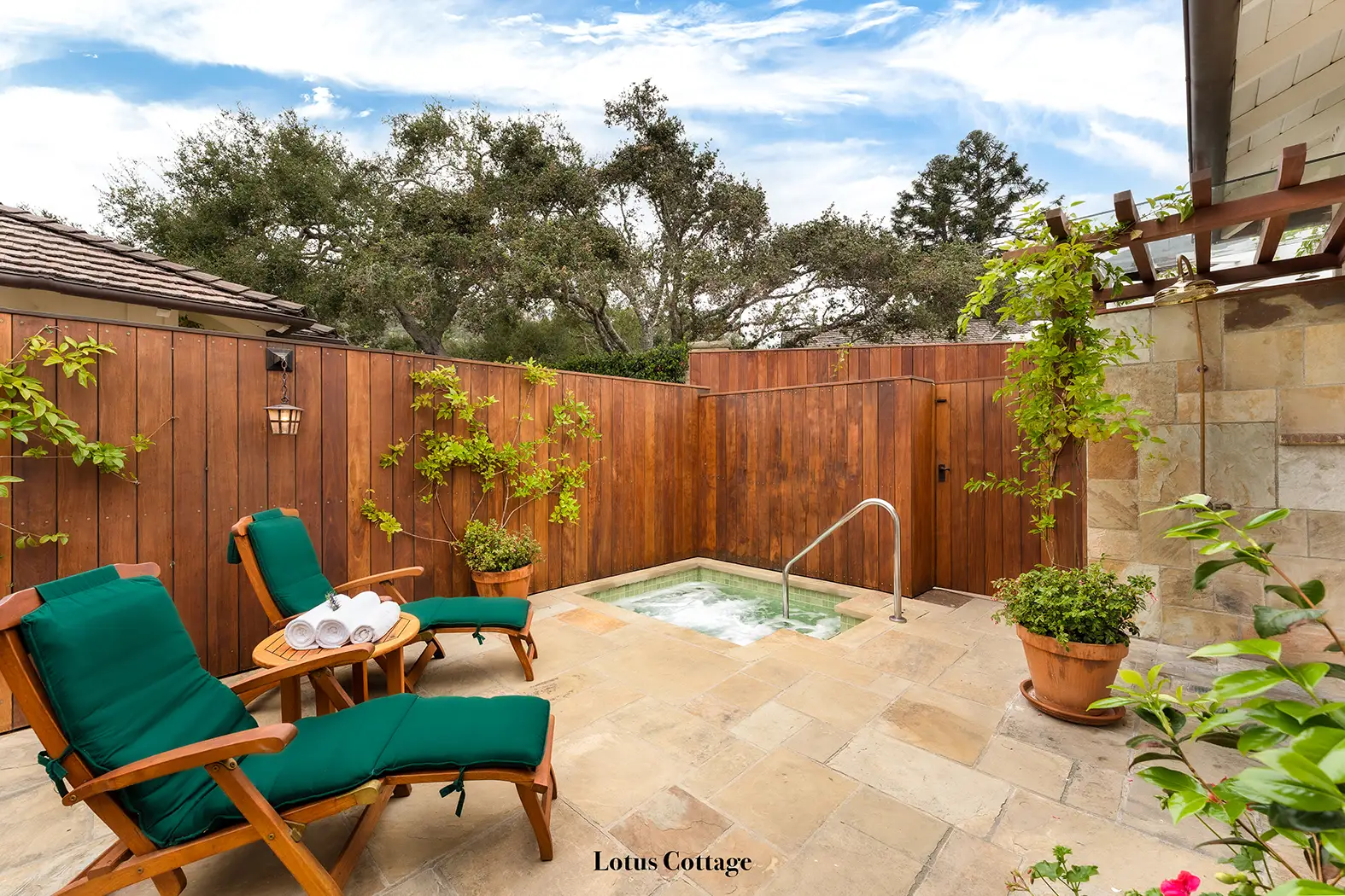 Lotus: the patio enclosed by a timber fence, with 2 green loungers and the sunken spa.
