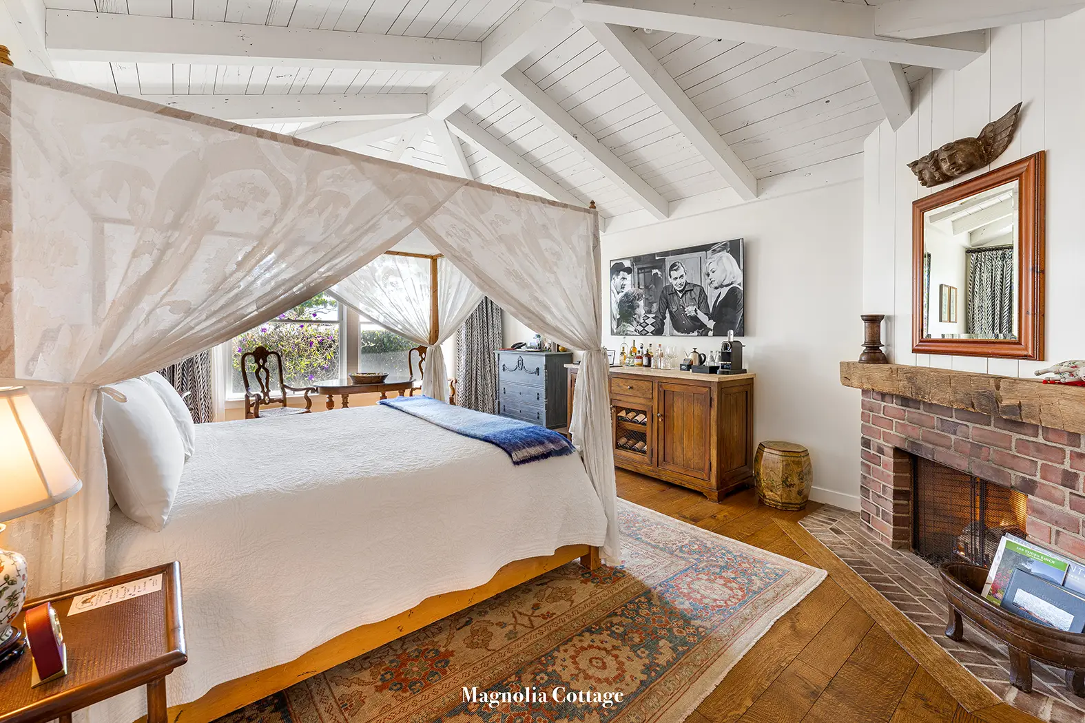 Magnolia: the canopy bed under a white trussed ceiling, the brick fireplace in the corner.