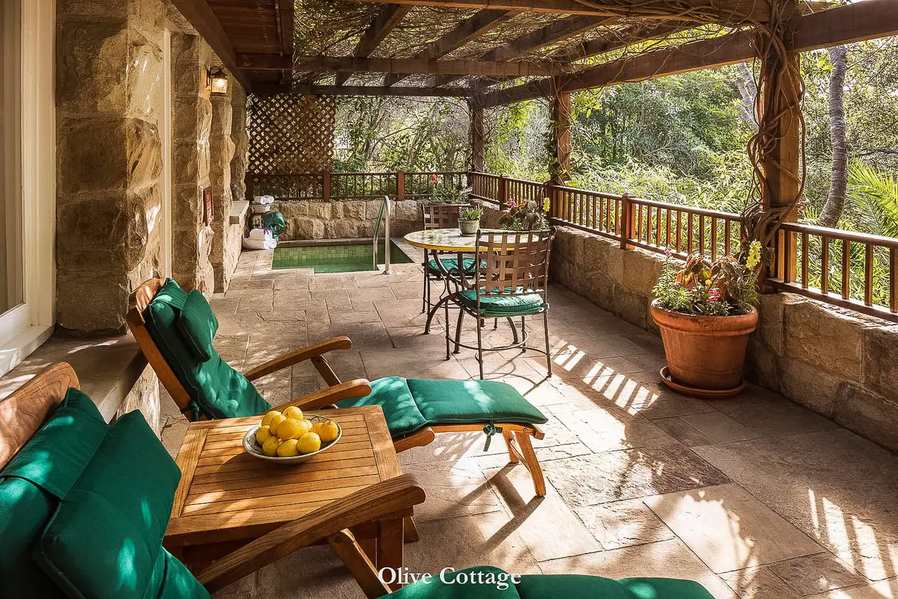 Olive: the stone veranda under a pergola, with green loungers, a small table and trees beyond the rail.
