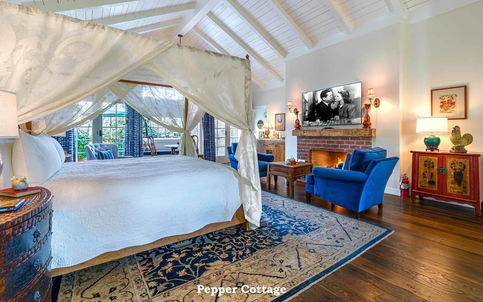 Pepper: the canopy bed on a blue rug and blue armchairs before the lit brick fireplace.