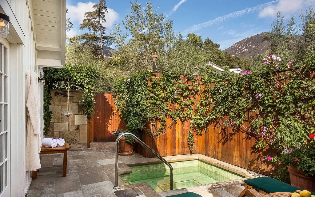 Rose: the patio with its sunken spa and stone outdoor shower, a fence covered in climbers and a mountain behind.