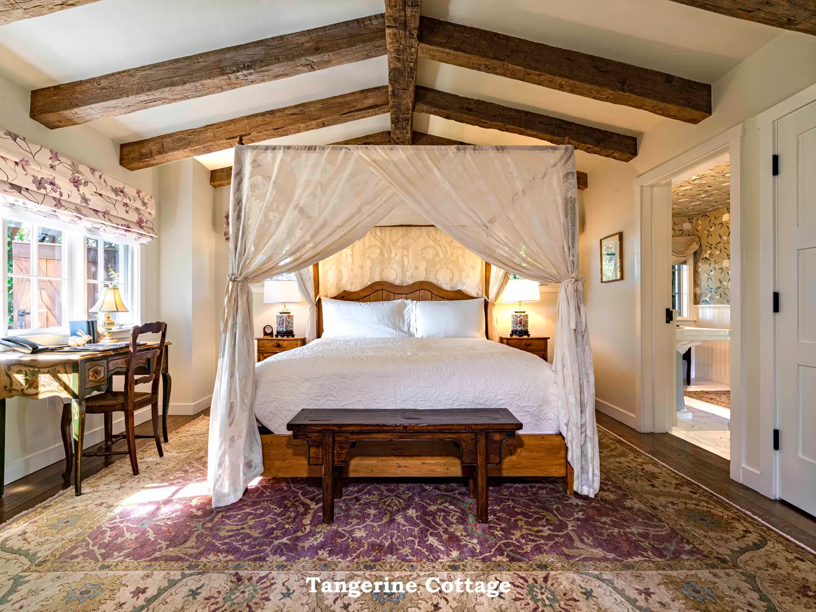 Tangerine: the canopy bed under dark beams, a bench at its foot and a desk by the window.