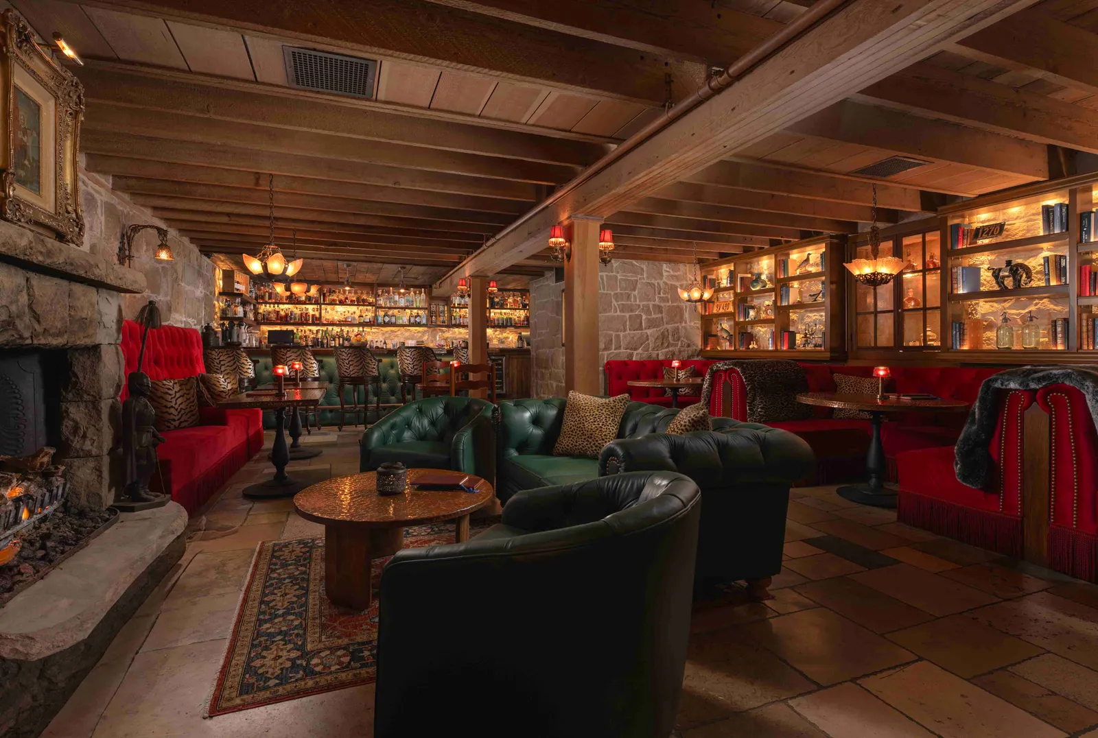 The Speakeasy’s room: a stone fireplace, green leather armchairs, red banquettes and lit shelves under the beams.