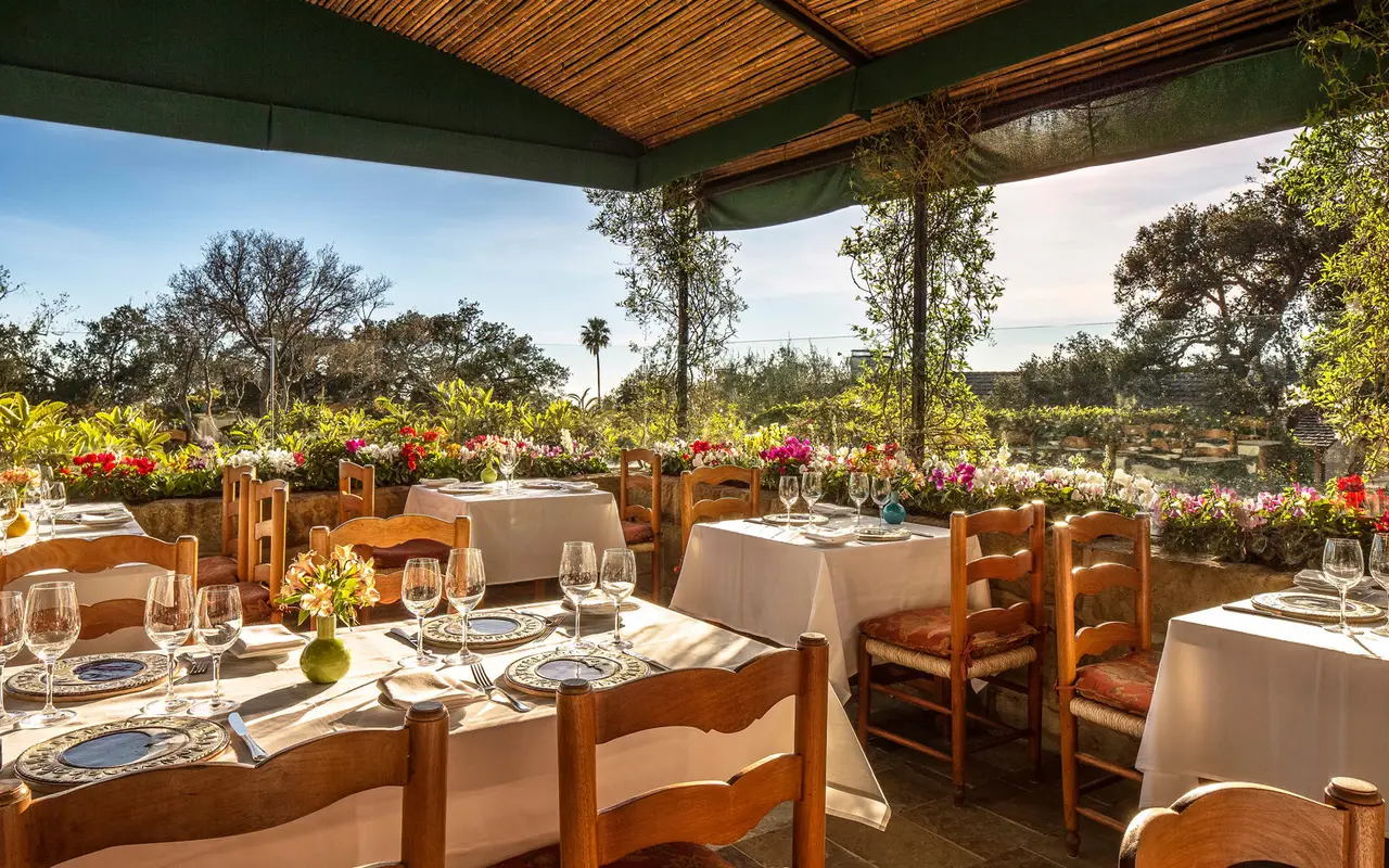 Stonehouse’s covered terrace by day: white-clothed tables, rush-seated chairs, flower boxes and trees beyond the rail.