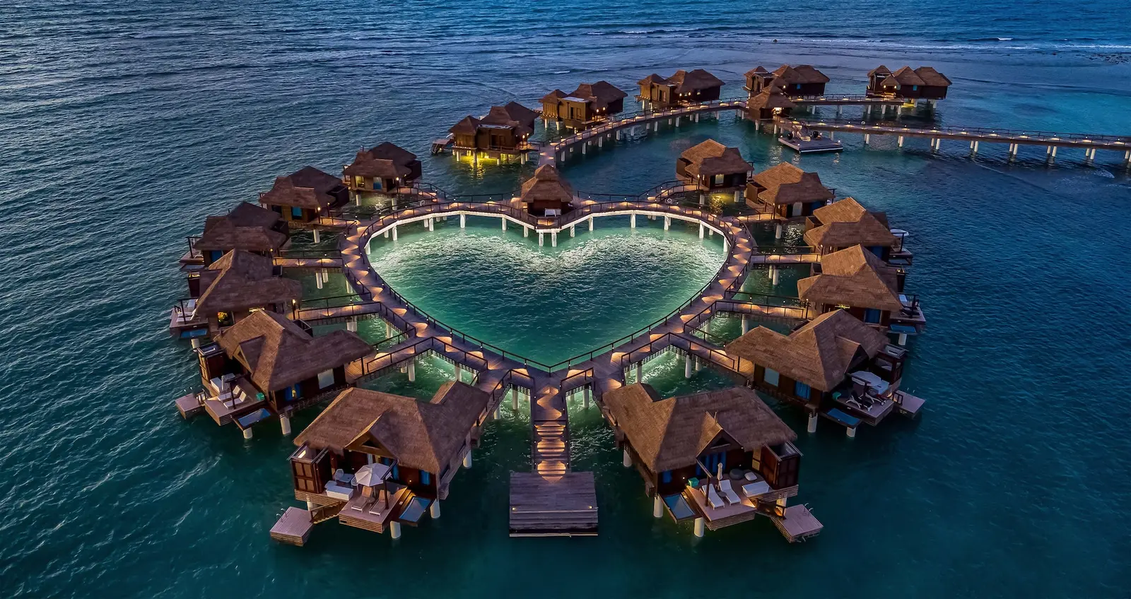 Official photograph, from before the reopening: the over-water bungalows at dusk, lit round the heart-shaped lagoon.