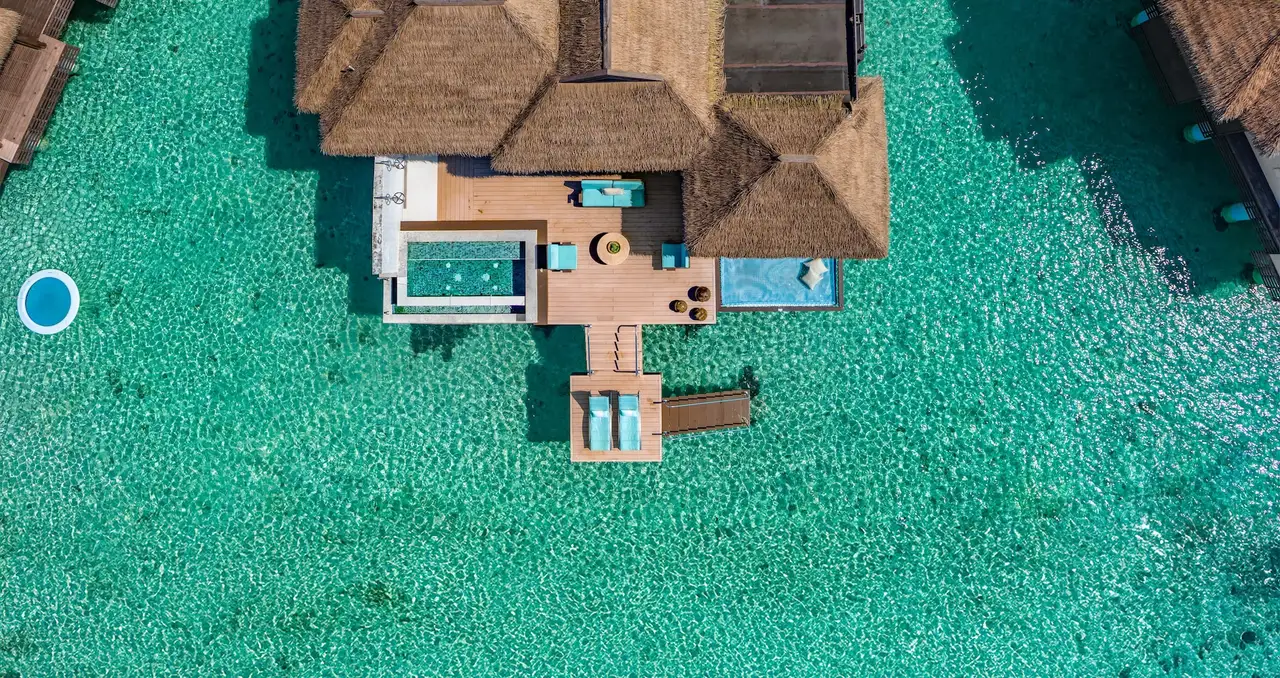 Official photograph, from before the reopening: an over-water villa seen from directly above, its thatched roof, the pool on the deck and the net slung over the sea.
