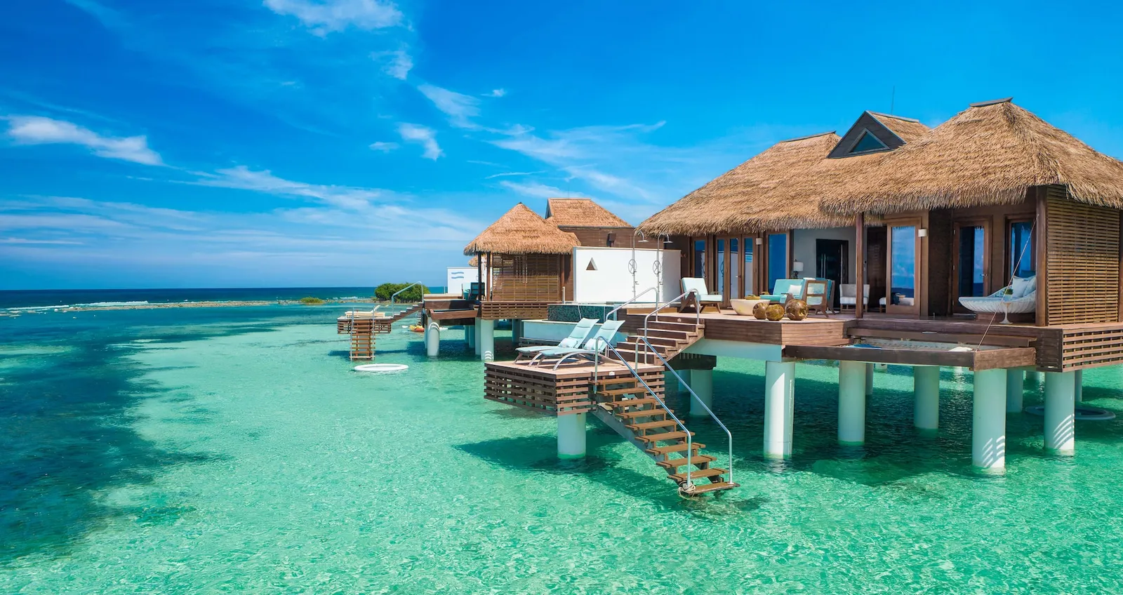 Official photograph, from before the reopening: an over-water villa seen from the sea, with steps down to the water, its deck and the hammock slung over the sea.