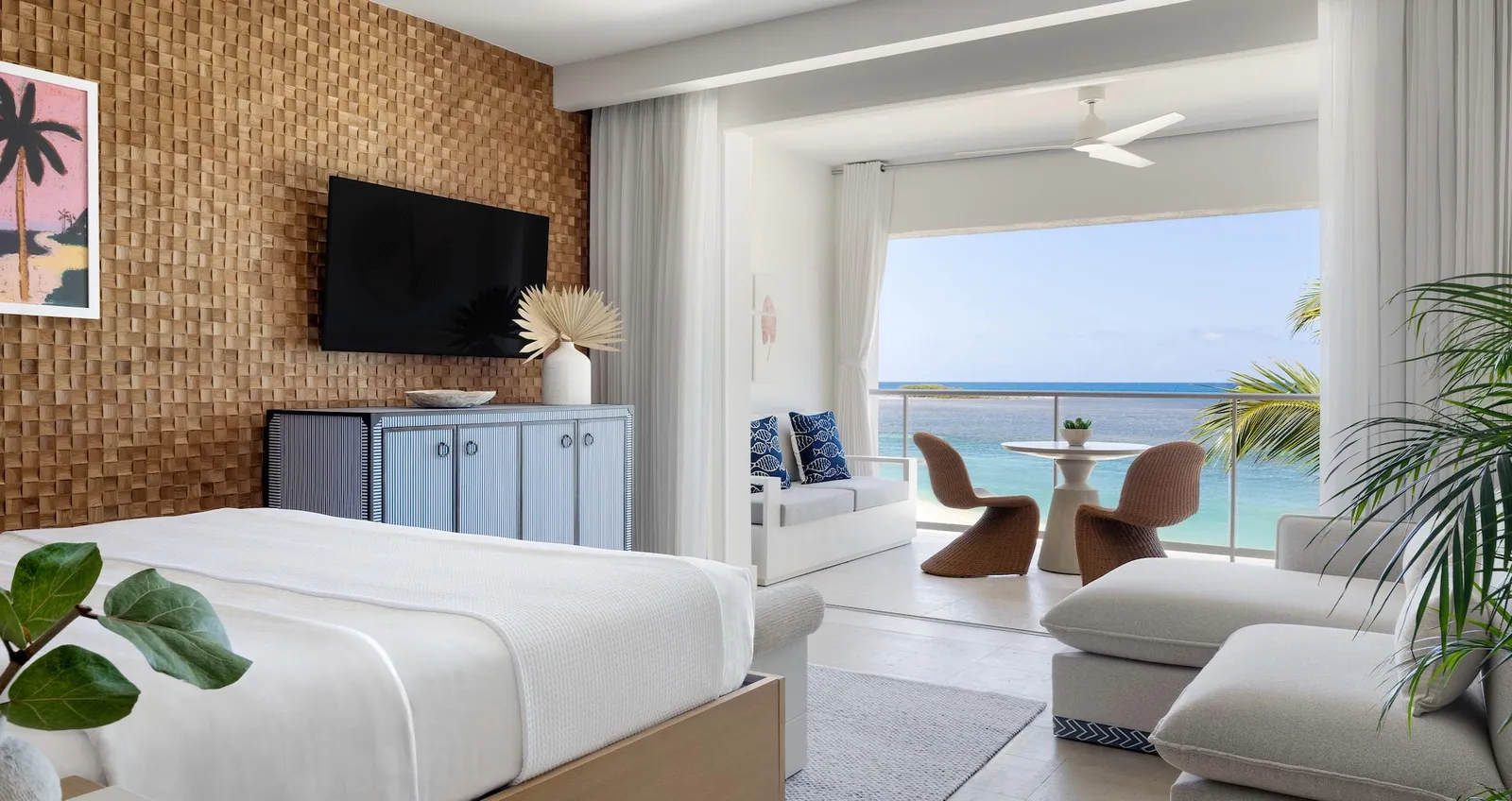 Official image: a bedroom with a woven timber wall panel, a sitting area and a balcony over the sea.