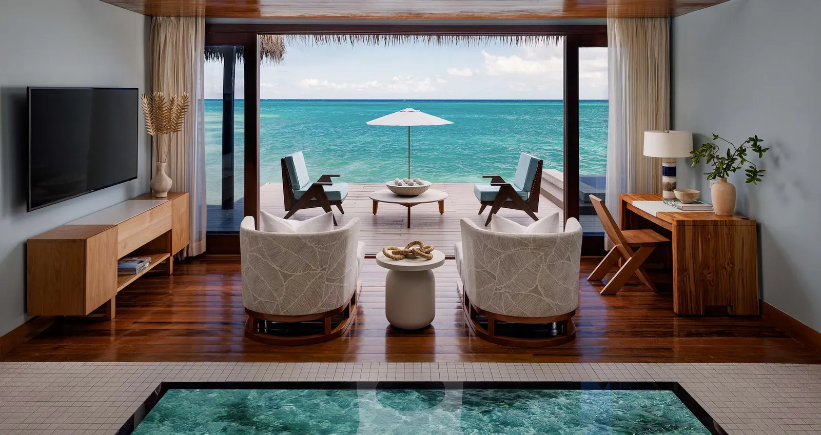 Official photograph, from before the reopening: an over-water villa’s living room, with its glass floor and the deck open to the sea.