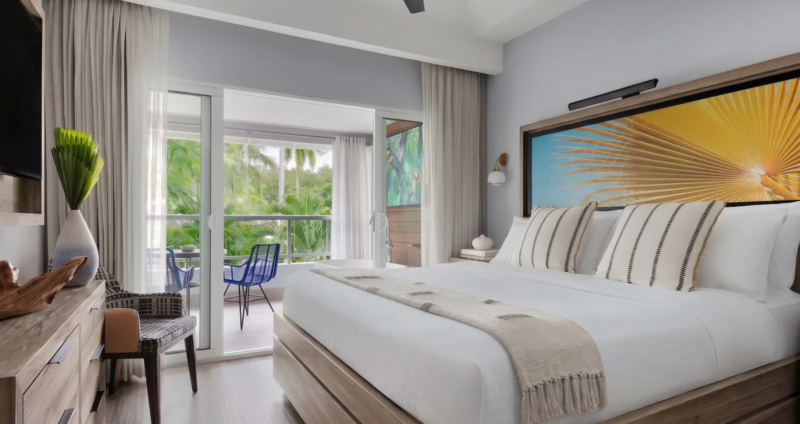 Official image: a bedroom with a king bed, a headboard painted with a yellow palm fan and glass doors to the balcony.