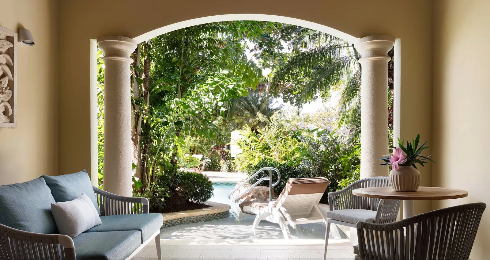 Official image: an arched patio with a sofa and table, giving onto the lagoon pool among the plants.