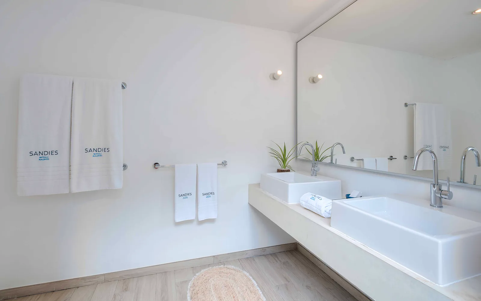 A beach bungalow bathroom, with its white double basin, the mirror and towels bearing the resort’s name.