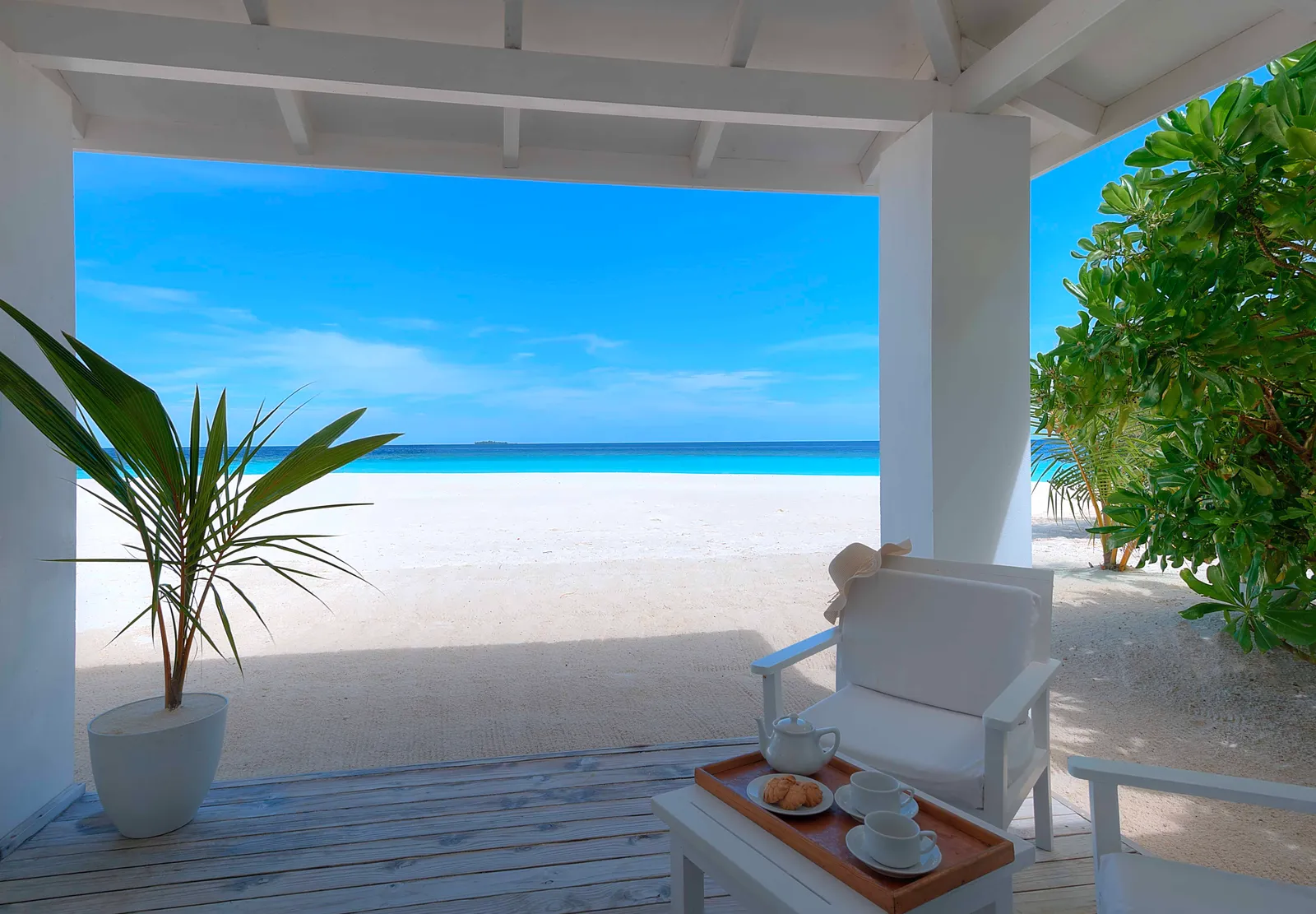 A beach bungalow’s veranda: a white armchair, a tray of tea and, beyond the columns, the sand and the sea.