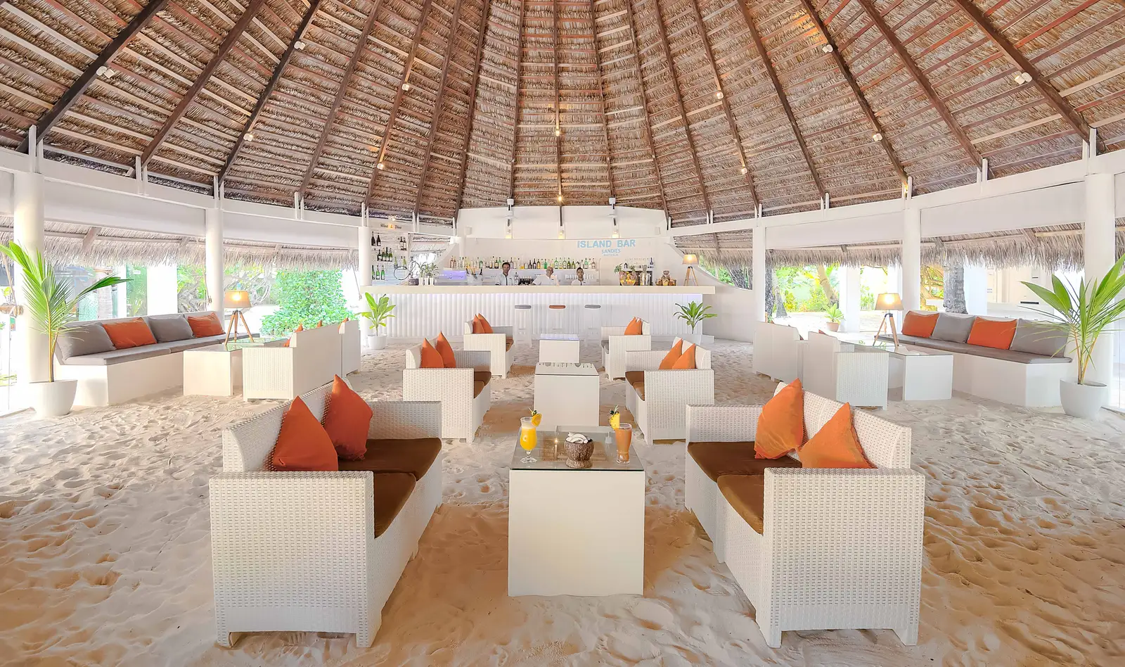The Island Bar under its great thatched roof, white sofas and orange cushions on a sand floor.