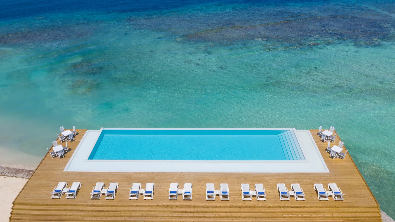 The pool from above, on its wooden deck, with the loungers in a row and the lagoon around it.