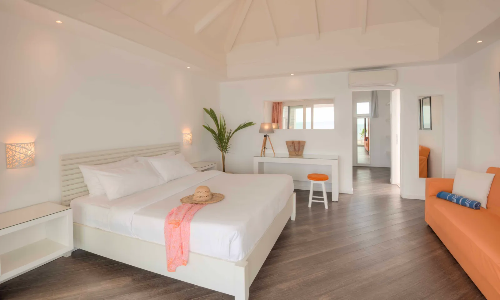 A water villa bedroom, with its white bed, dark parquet and the orange sofa bed.