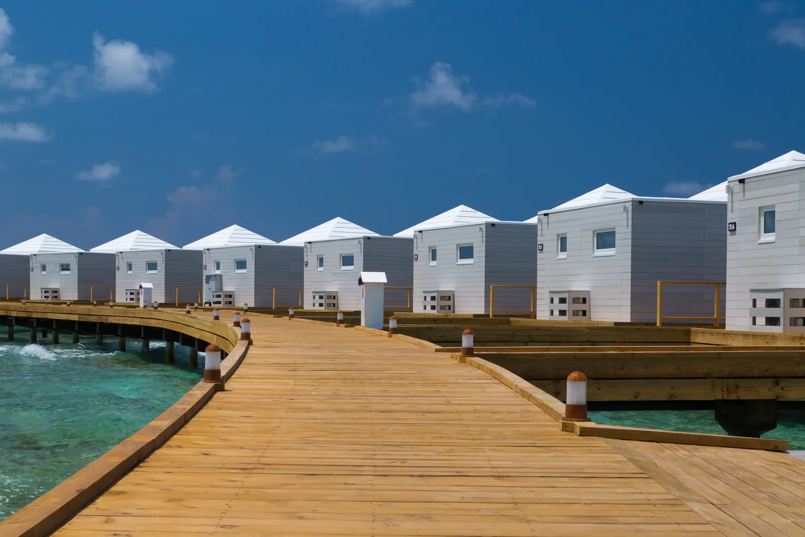 The wooden jetty to the water villas, white with pointed roofs, in a row above the lagoon.