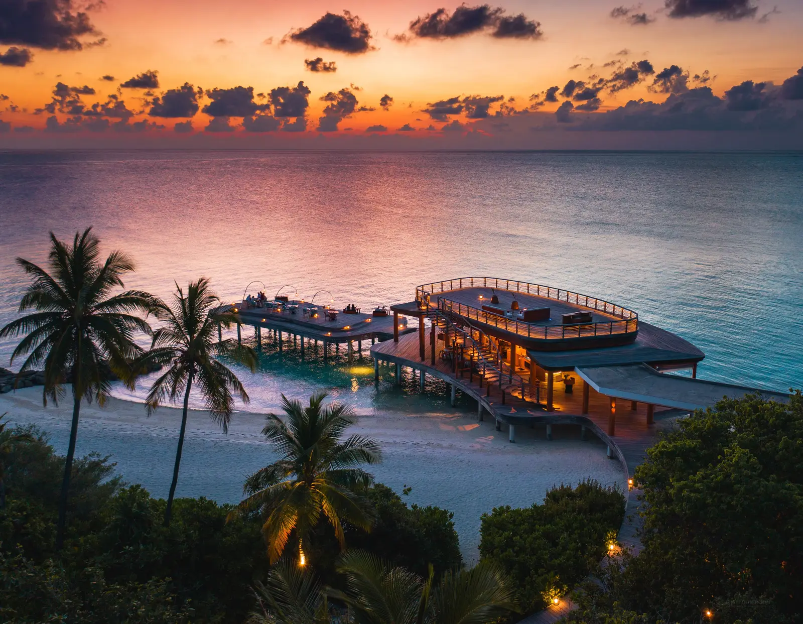 Kata, the Japanese restaurant over the water, lit up at sunset behind the palms.