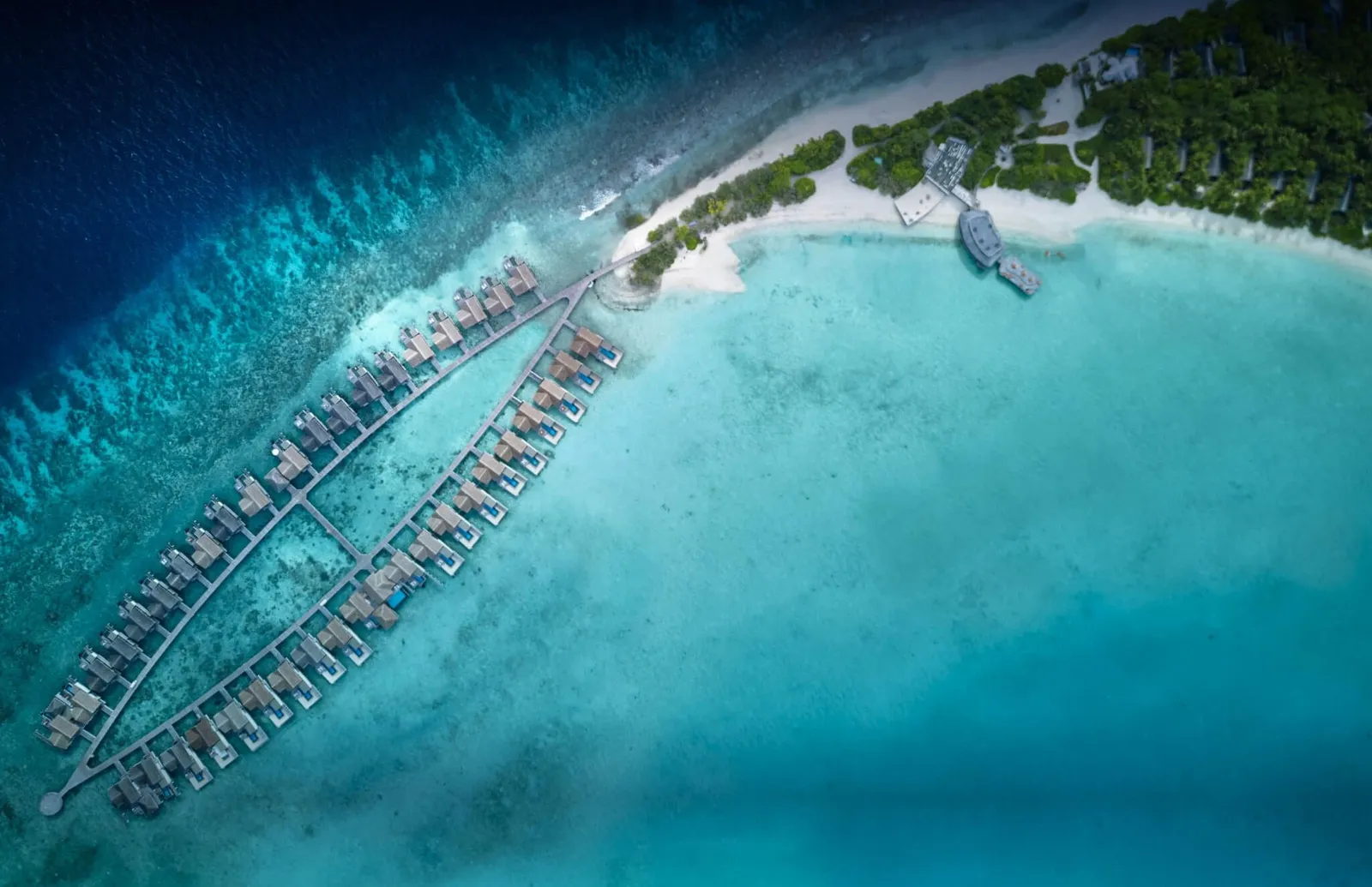 The water villas in rows along their jetties, seen from above over the edge of the lagoon and the reef.