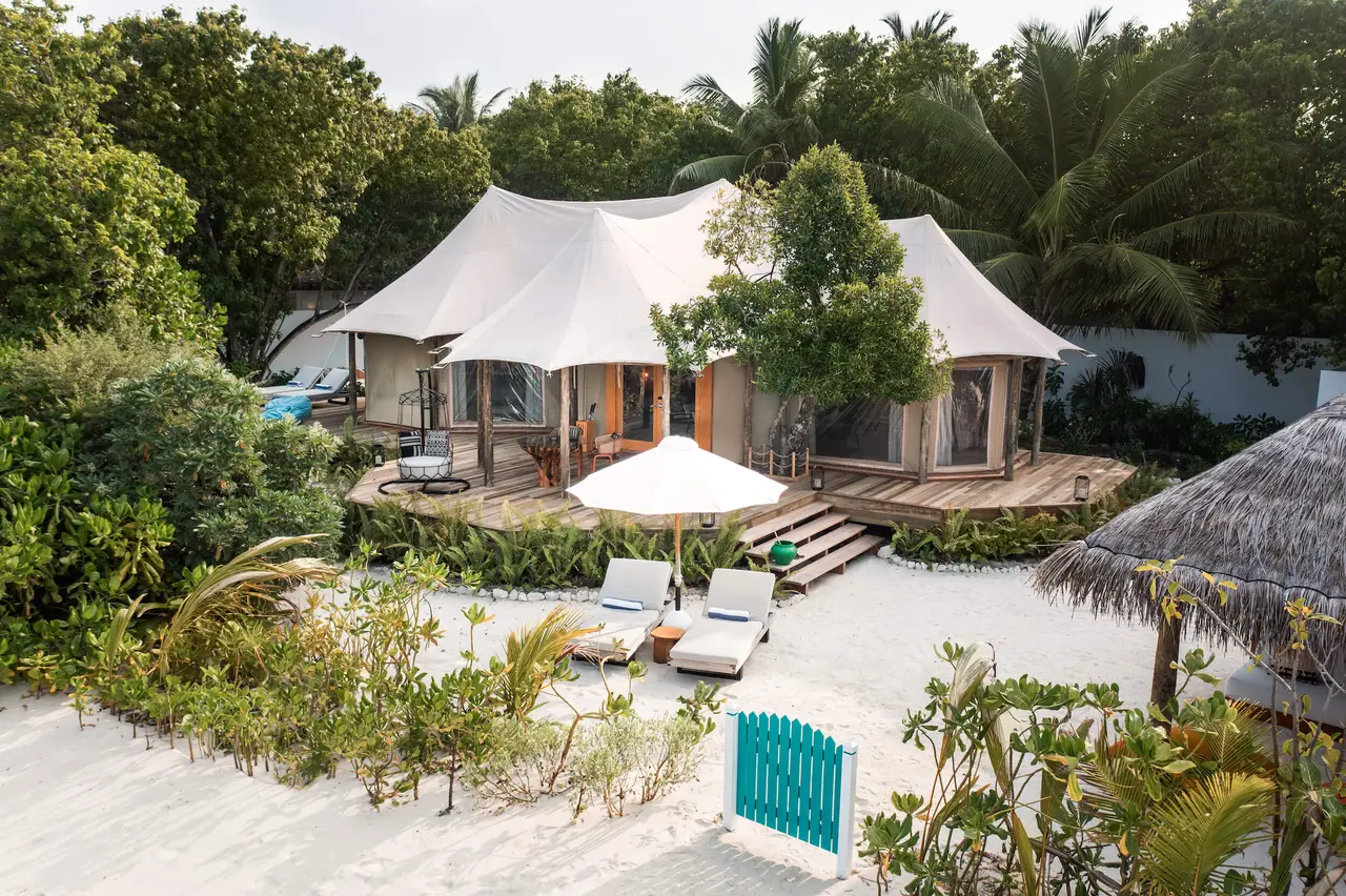 A Safari Tented Beach Villa: the white tent among the trees, its deck with loungers and a gate onto the beach.
