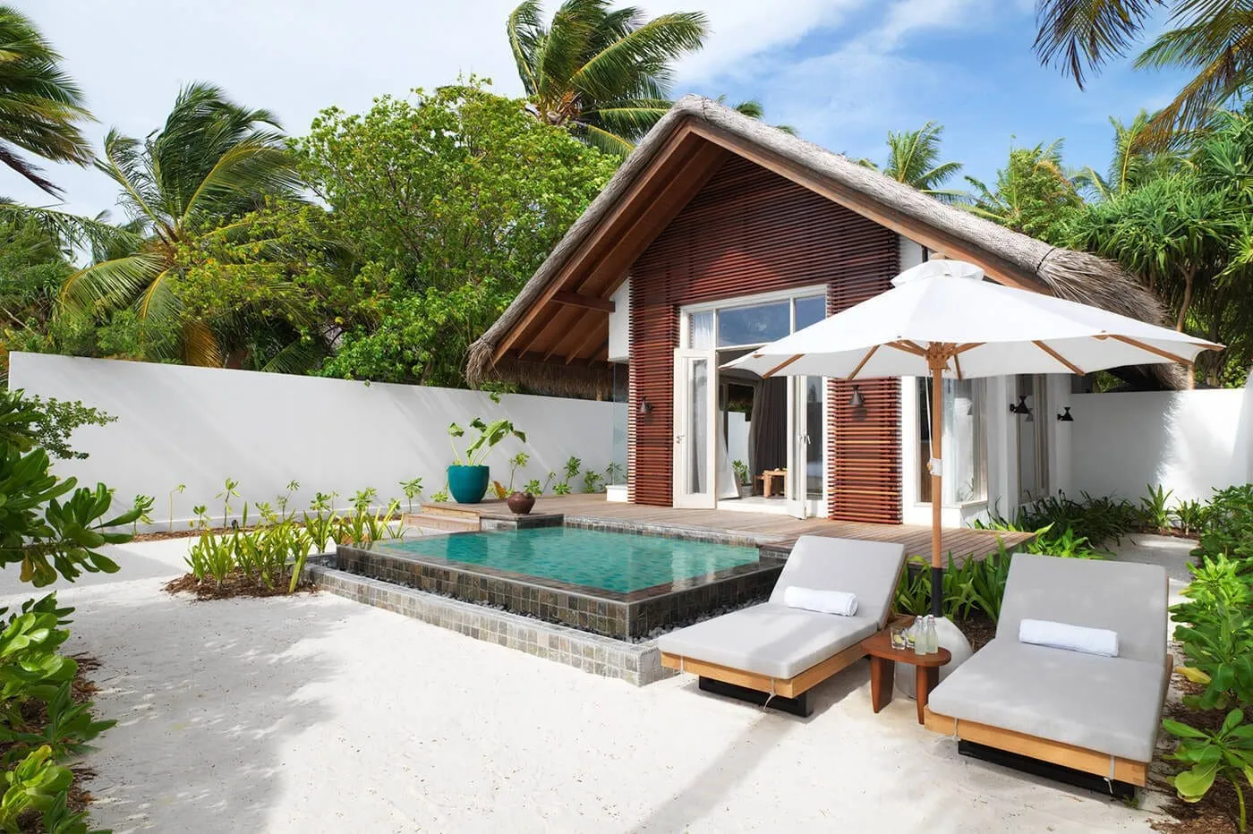 A Sunset Beach Villa: the thatched villa, its pool and 2 loungers in the sandy courtyard.