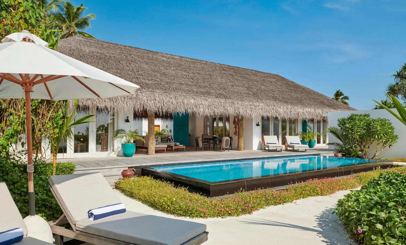 A Three Bedroom Sunset Beach Villa: the long pool, the loungers and the villa under its thatched roof.