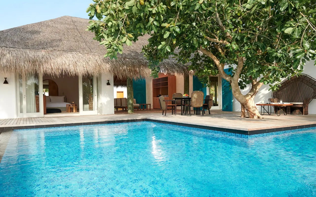 A Two Bedroom Sunset Beach Villa’s pool, with the thatched villa and a tree on the terrace.