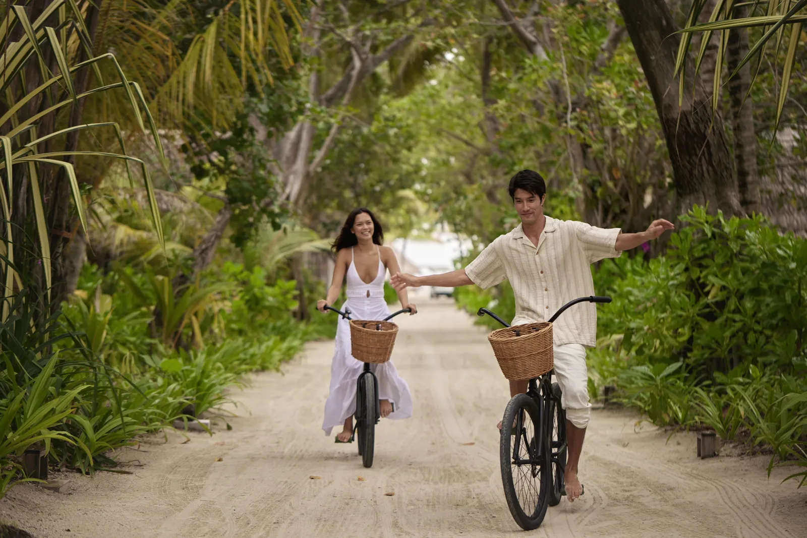 2 guests cycling along a sandy path between the trees