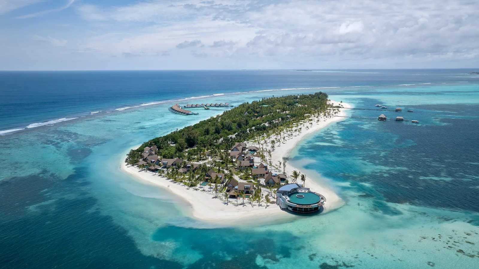 Kanuhura from the air: the green island edged with white sand, The Point’s round pool on the tip and the water villas at the far end of the lagoon