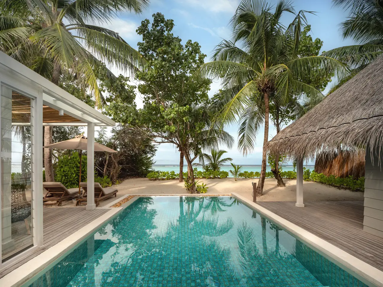 A Deluxe Beach Villa Suite’s pool, with the timber deck, the palms and the sea beyond