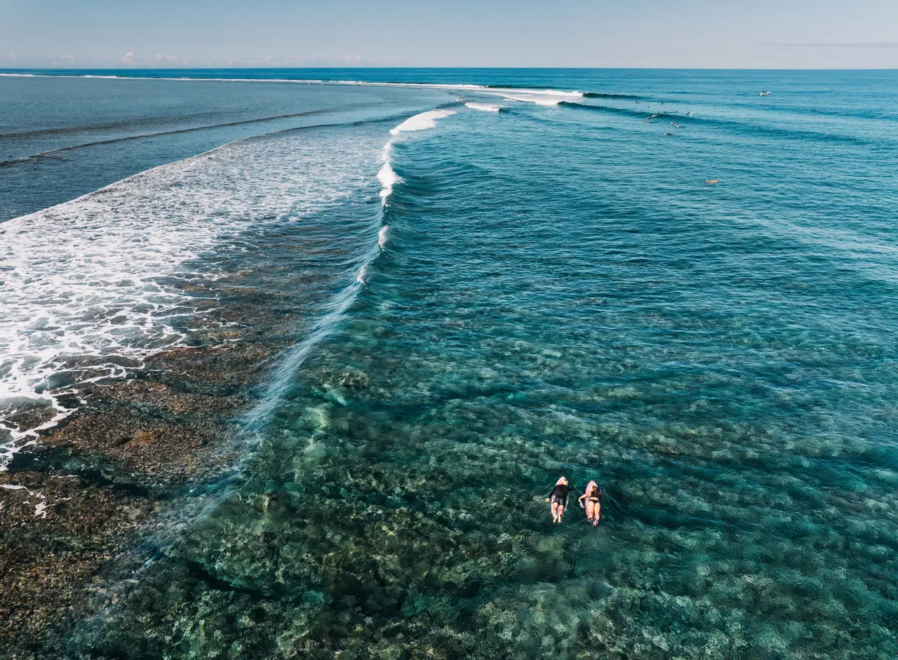 A wave breaking on the reef from the air, 2 surfers in the water