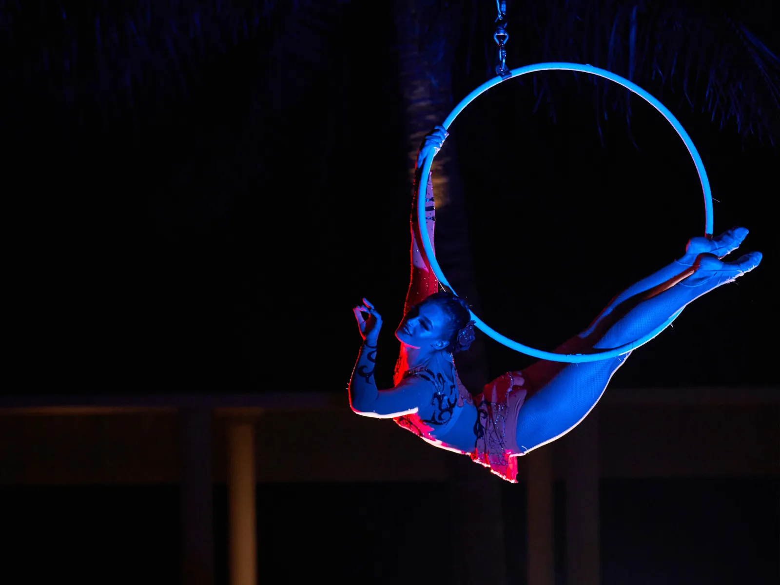 An acrobat hanging from a lit hoop at night
