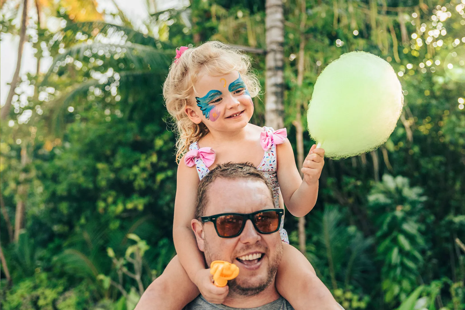 A girl with a painted face on her father’s shoulders, holding candyfloss