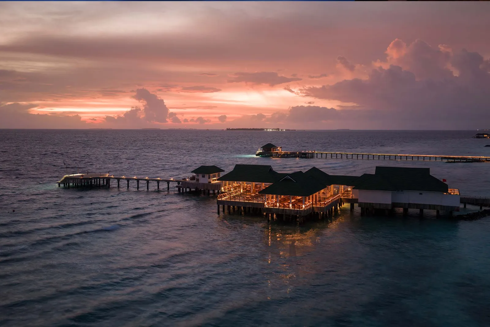 Takrai over the water at sunset, its lights on along the jetty