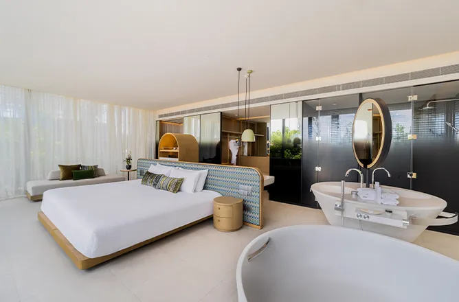 Open-plan bed, white freestanding bath and twin circular sinks within one glass-fronted room.