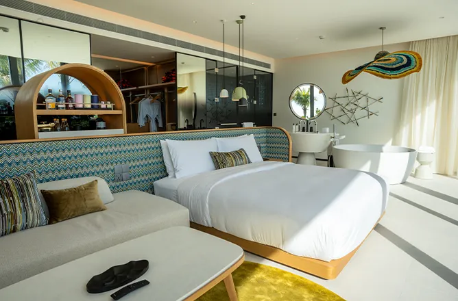 King bed and sofa beside open bath/double sinks, view to greenery.