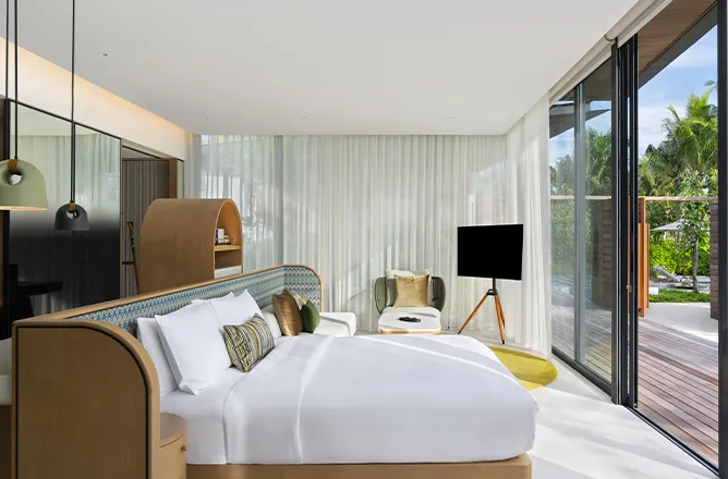 Bed and chair in glass-fronted room opening to planted terrace.