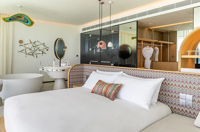 Bed beside open bathroom and wardrobe with colourful wave artwork.
