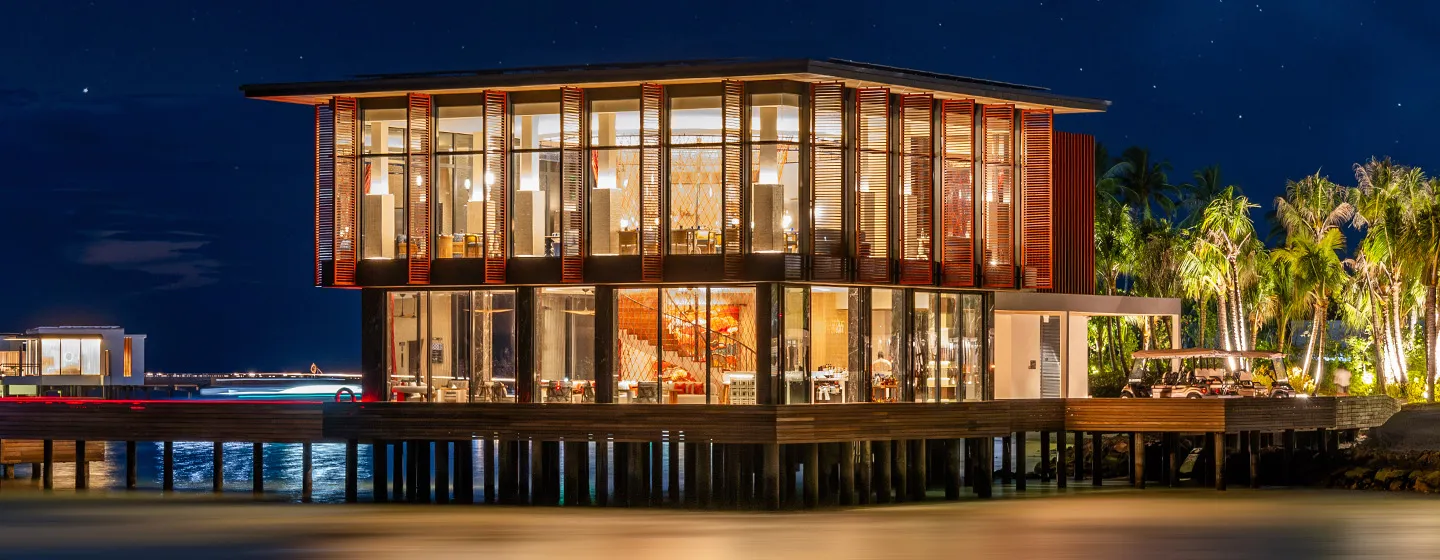 The illuminated Pavilion with a glass façade and an overwater walkway.