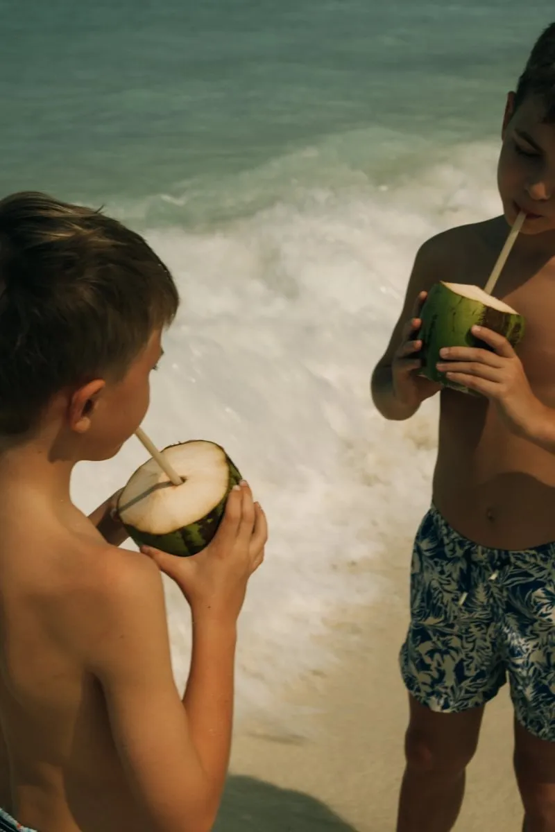 2 children at the water’s edge drinking from a coconut