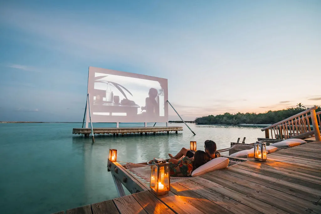 Cinema Paradiso at dusk: the screen over the lagoon, cushions and lanterns on the jetty
