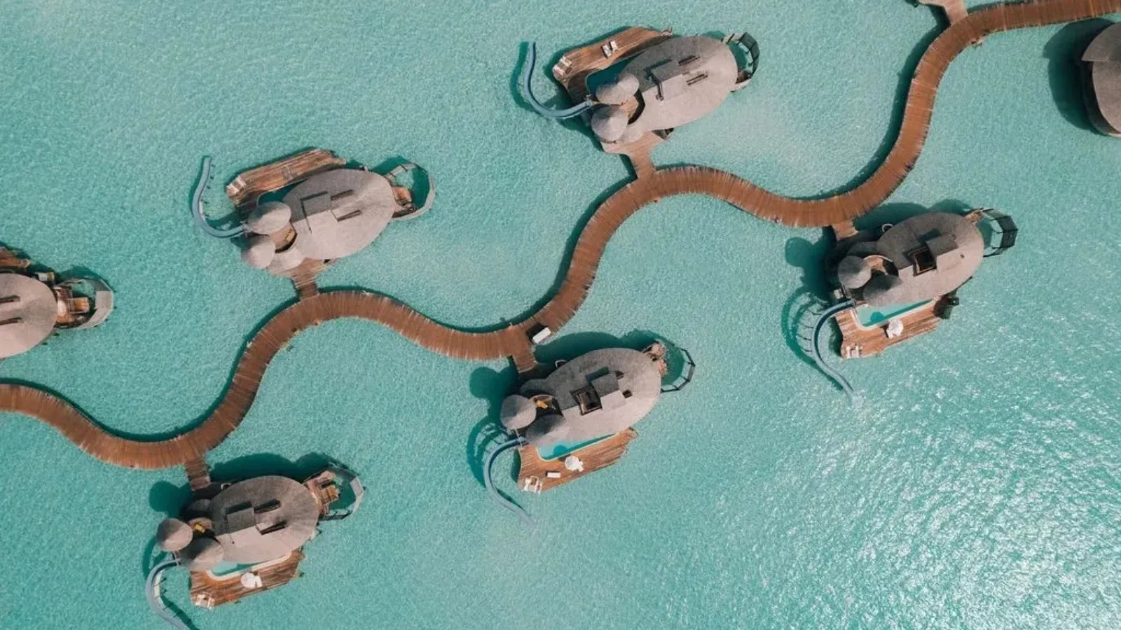 The villas over the turquoise lagoon from above, linked by a curving timber walkway