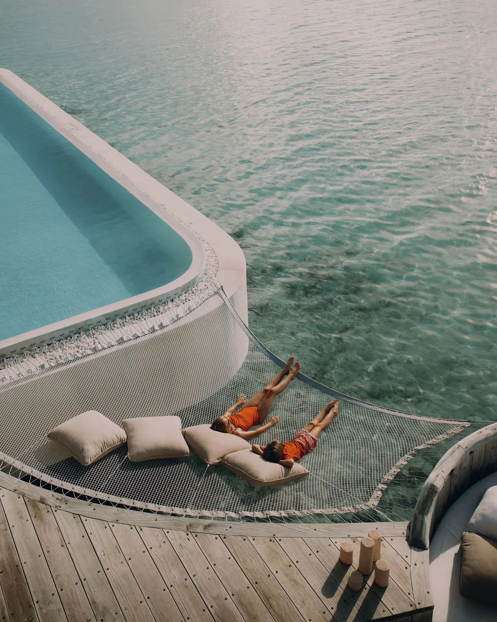 2 people on the net slung over the water beside the edge of a villa pool