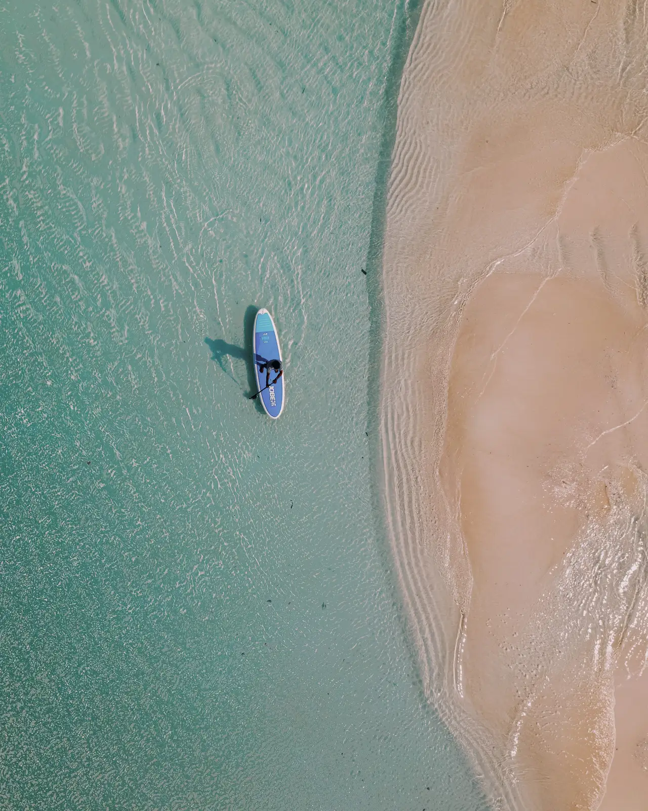 A paddleboard on turquoise water beside a tongue of sand