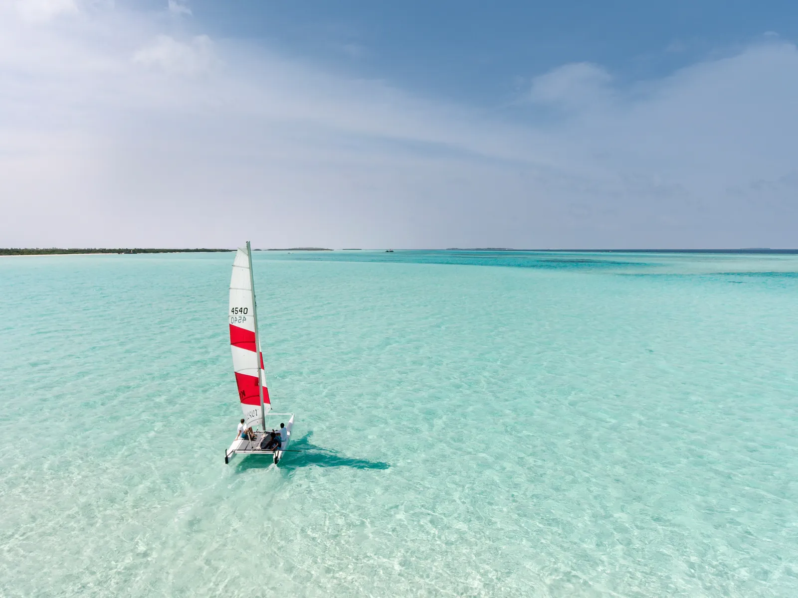 A small catamaran sailing on the clear, shallow lagoon