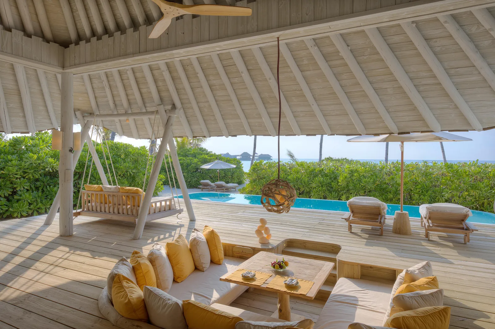 The covered deck of a Beach Villa, with a swing seat, the sunken lounge and the pool among the plants.