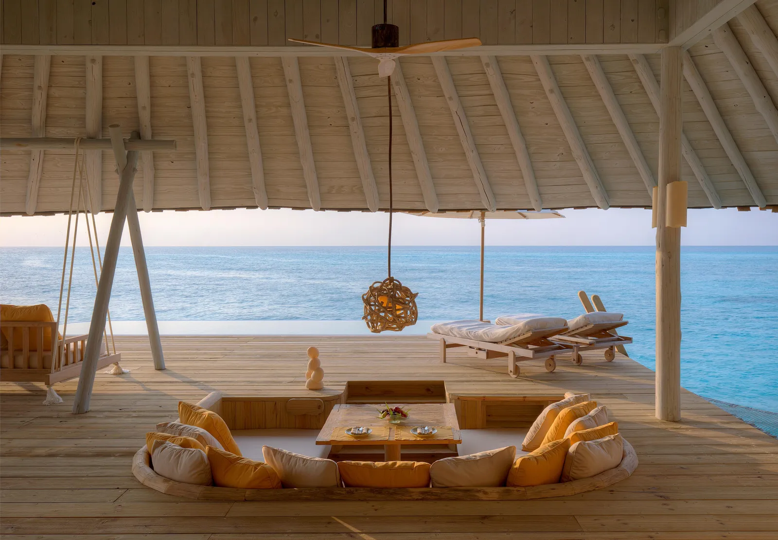 The sunken lounge on an overwater villa’s deck, with yellow cushions, a swing seat and the open sea ahead.